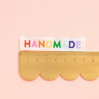 Scallop-edged ruler with 'HANDMADE' in colorful letters on a pink background