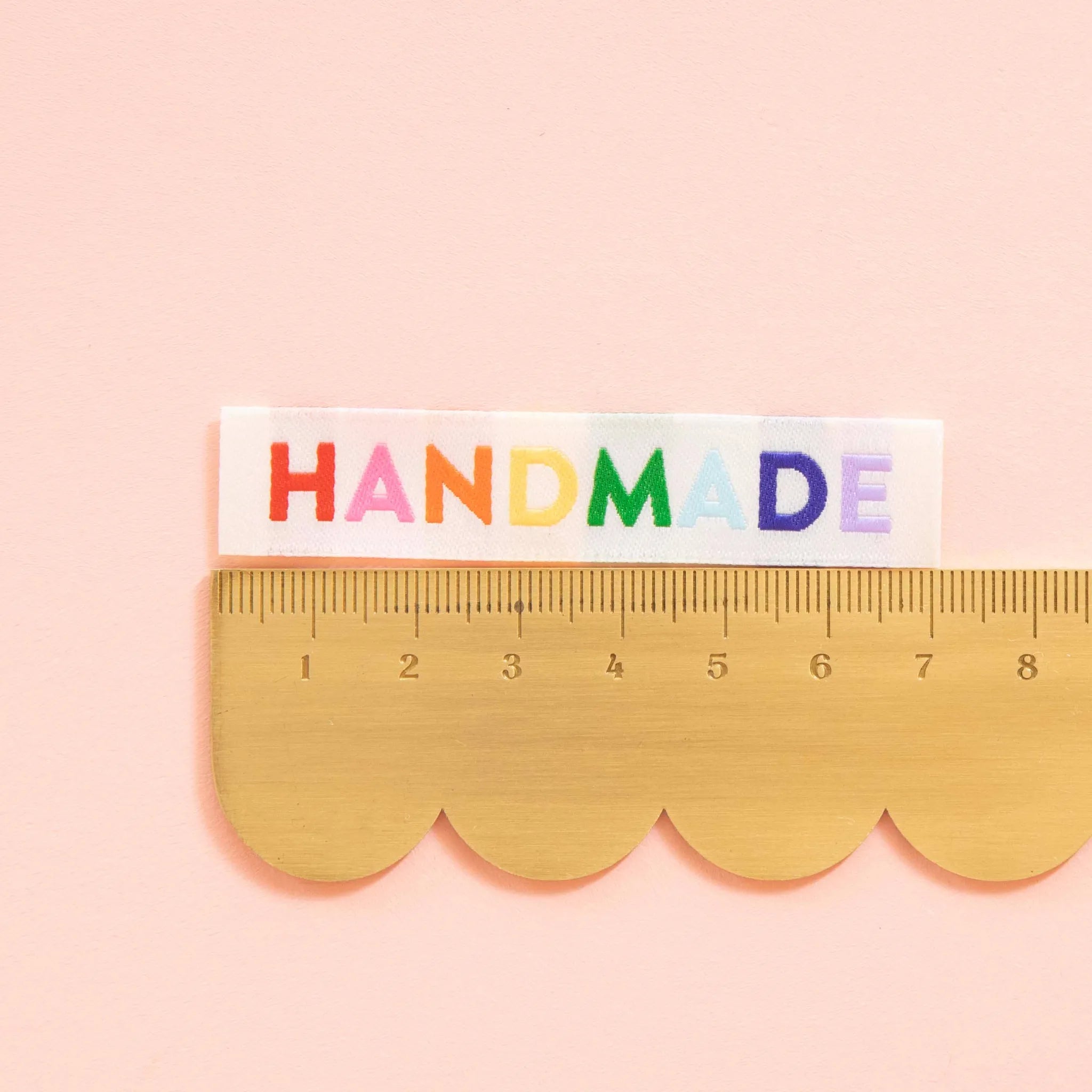 Scallop-edged ruler with 'HANDMADE' in colorful letters on a pink background