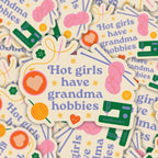 Sticker with 'Hot girls have grandma hobbies' text surrounded by colorful graphics on a patterned background.
