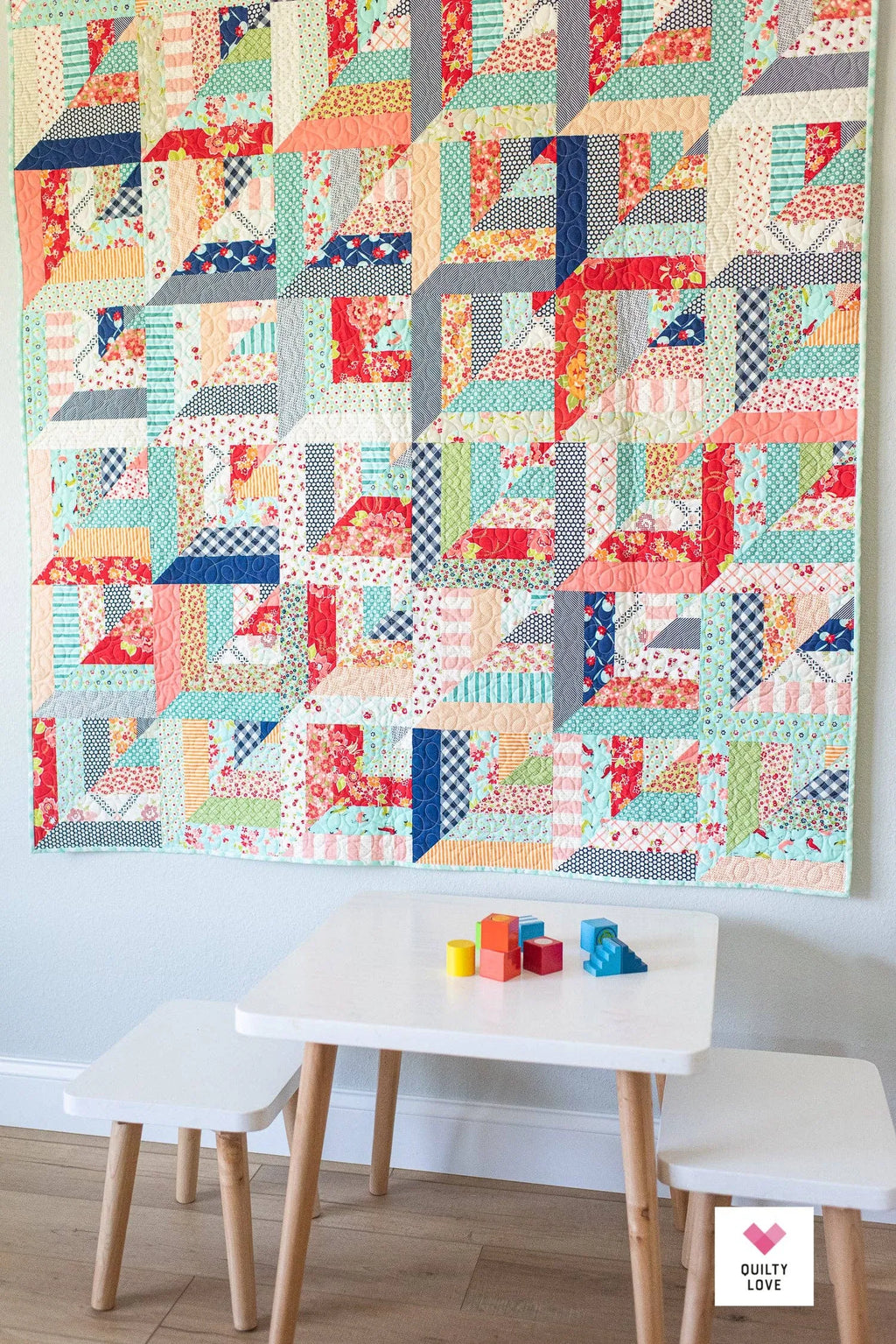 Colorful quilt hanging on a wall above a small table with children's toys. Lucky Log Cabin by Quilty Love