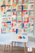 Colorful quilt hanging on a wall above a small table with children's toys. Lucky Log Cabin by Quilty Love