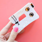 Hand holding a small sewing machine-like tool with eyelets on a pink background by Sarah Hearts