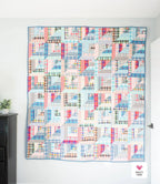 Colorful quilt with geometric pattern on a white wall Lucky Log Cabin by Quilty Love