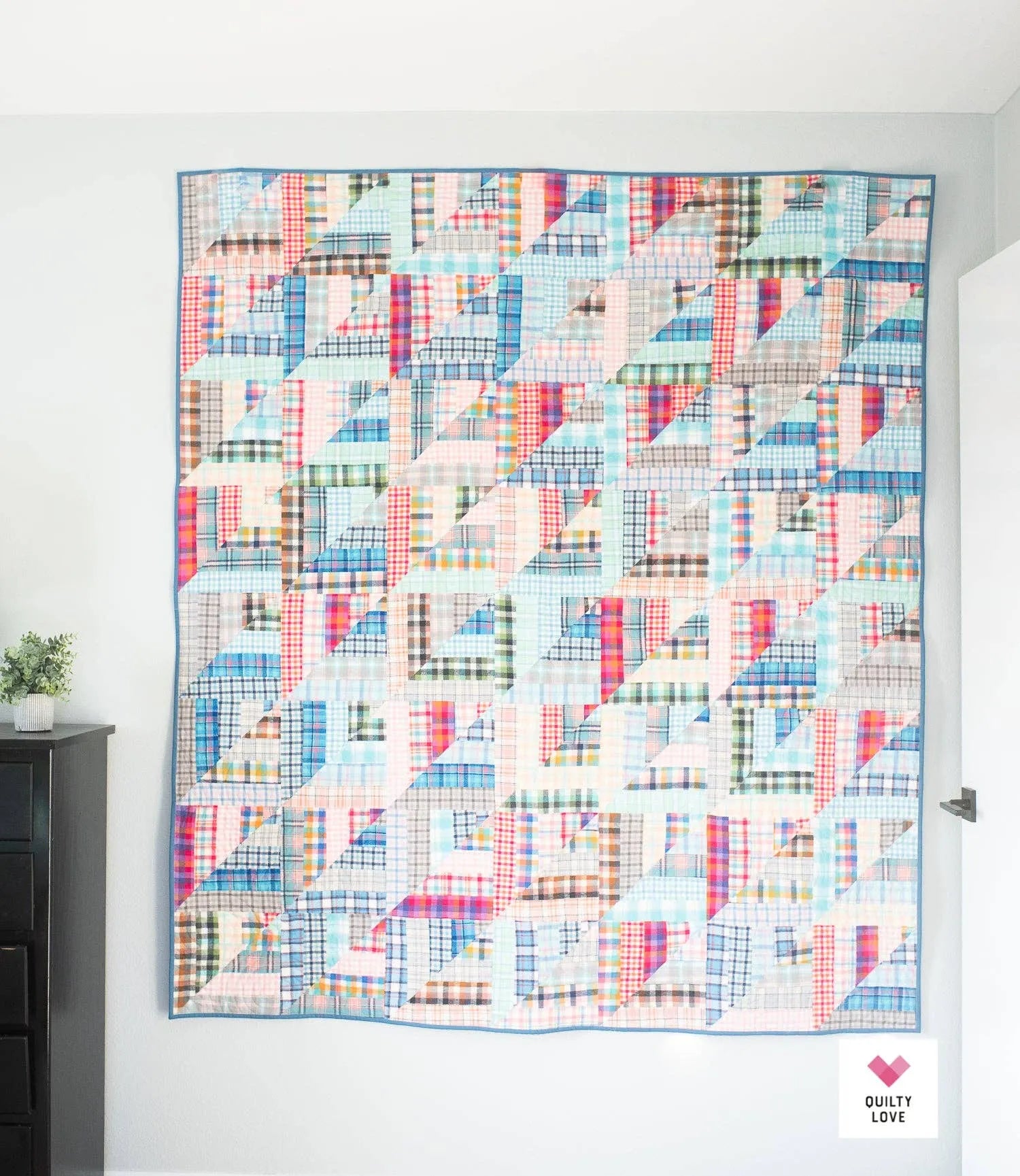 Colorful quilt with geometric pattern on a white wall Lucky Log Cabin by Quilty Love