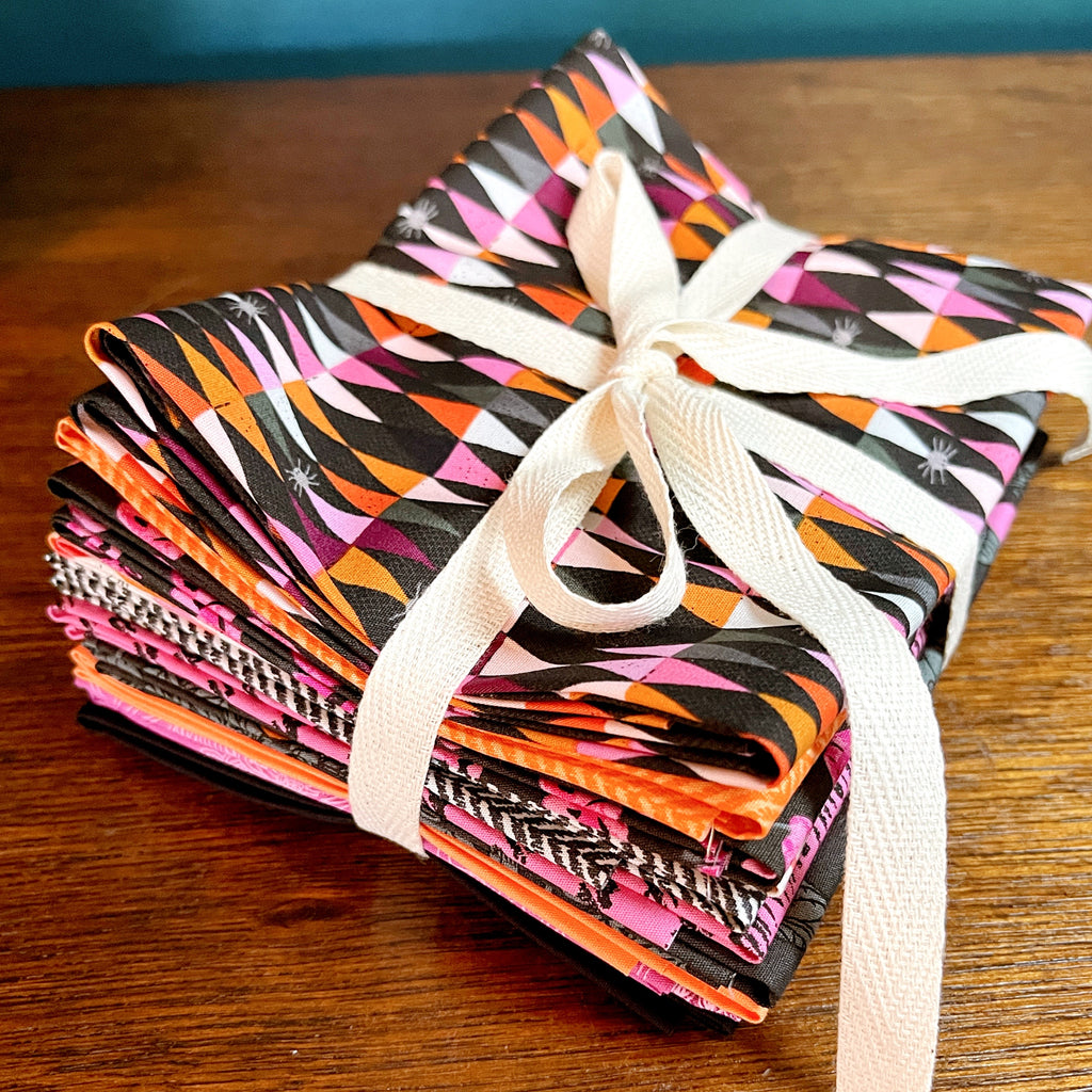 Stack of colorful fabric quilting cotton fat quarter bundles tied with a twill tape ribbon on a wooden surface