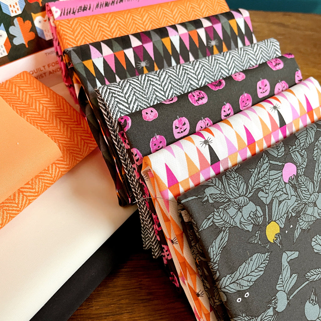 Stack of Halloween-themed fabric swatches on a wooden surface Enshadow Collection by Art Gallery Fabrics