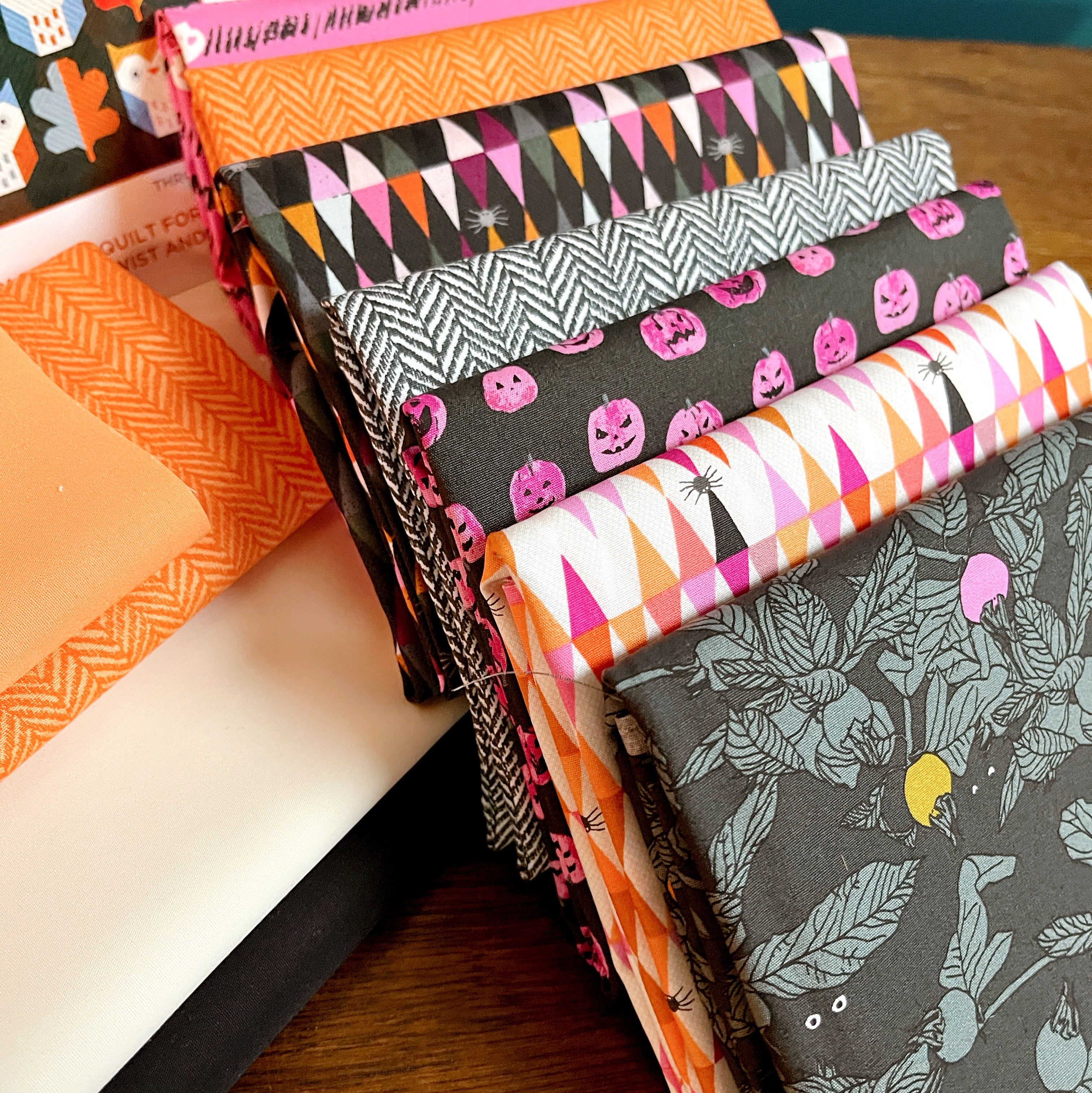 Stack of Halloween-themed fabric swatches on a wooden surface Enshadow Collection by Art Gallery Fabrics