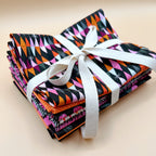 Stack of colorful quilting cotton fabric bundles tied with a white ribbon on a beige background