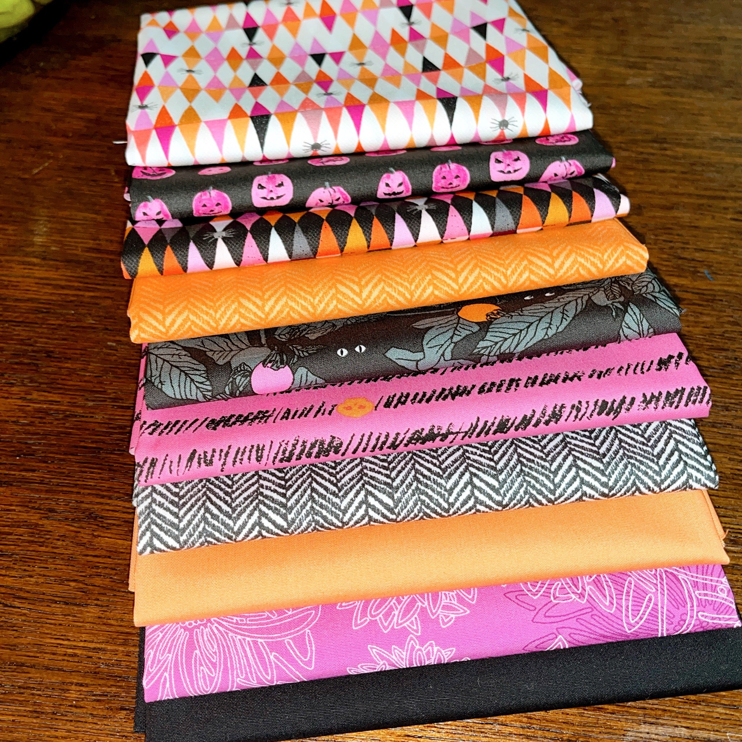 Enshadow Fat Quarter Bundle.  Stack of Halloween-themed fabric swatches on a wooden surface