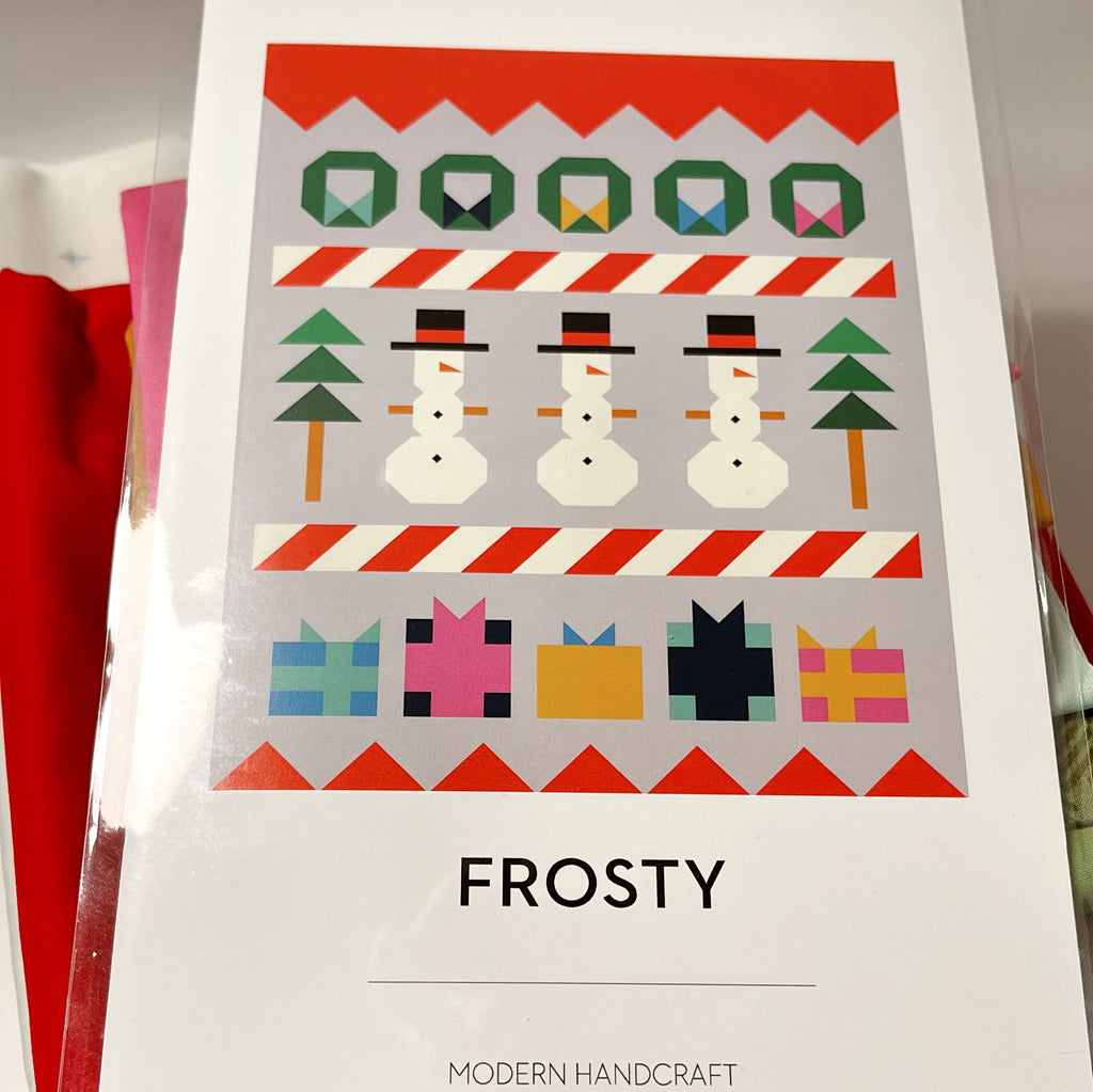 Close-up of the pattern cover:
“Modern Handcraft Frosty quilt pattern cover showing rows of wreaths, snowmen, evergreen trees, and colorful gifts.”