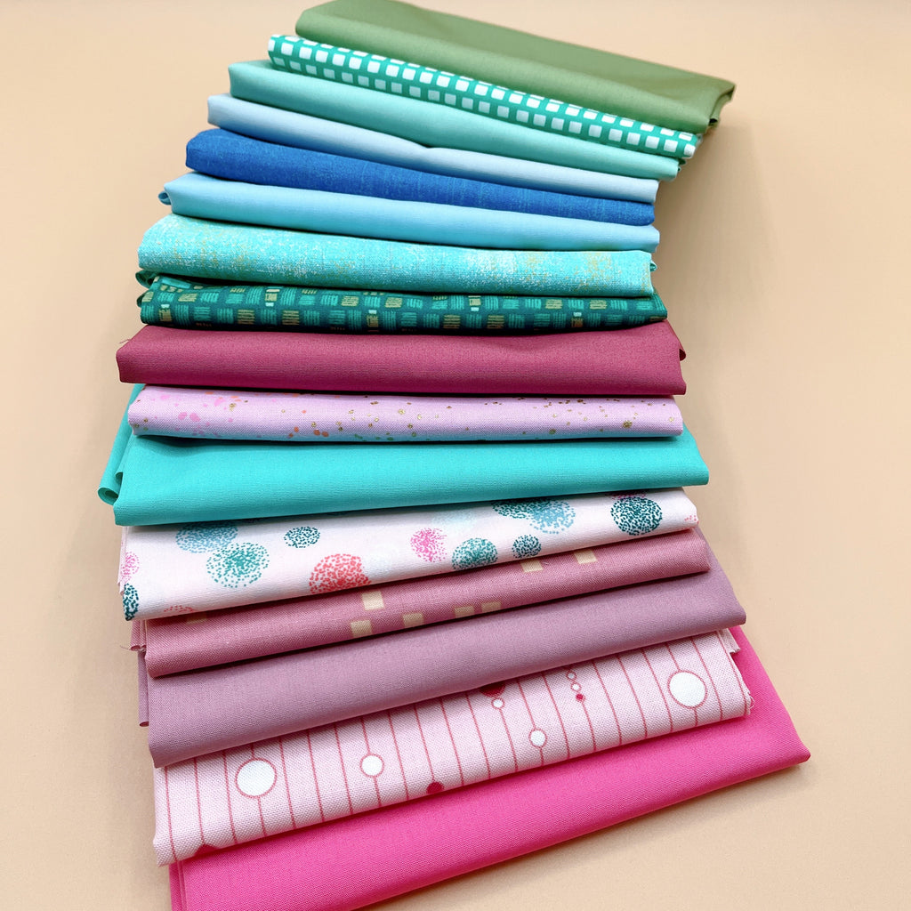 Stack of sixteen folded fat quarters on a peach background, from olive green and teal grid at the top through aqua, blue, and teal prints, then raspberry, lavender speckle, mauve, and dusty rose, down to hot pink at the bottom.