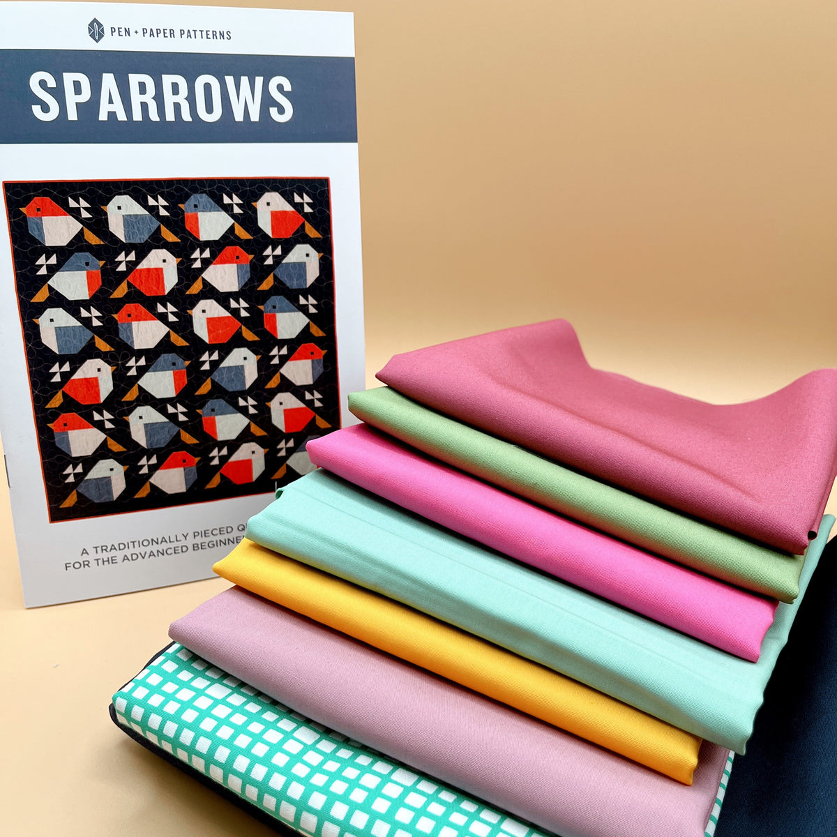 Sparrows quilt kit with pattern booklet and a stack of folded solid and grid-print fabrics in pink, green, mint, yellow and navy